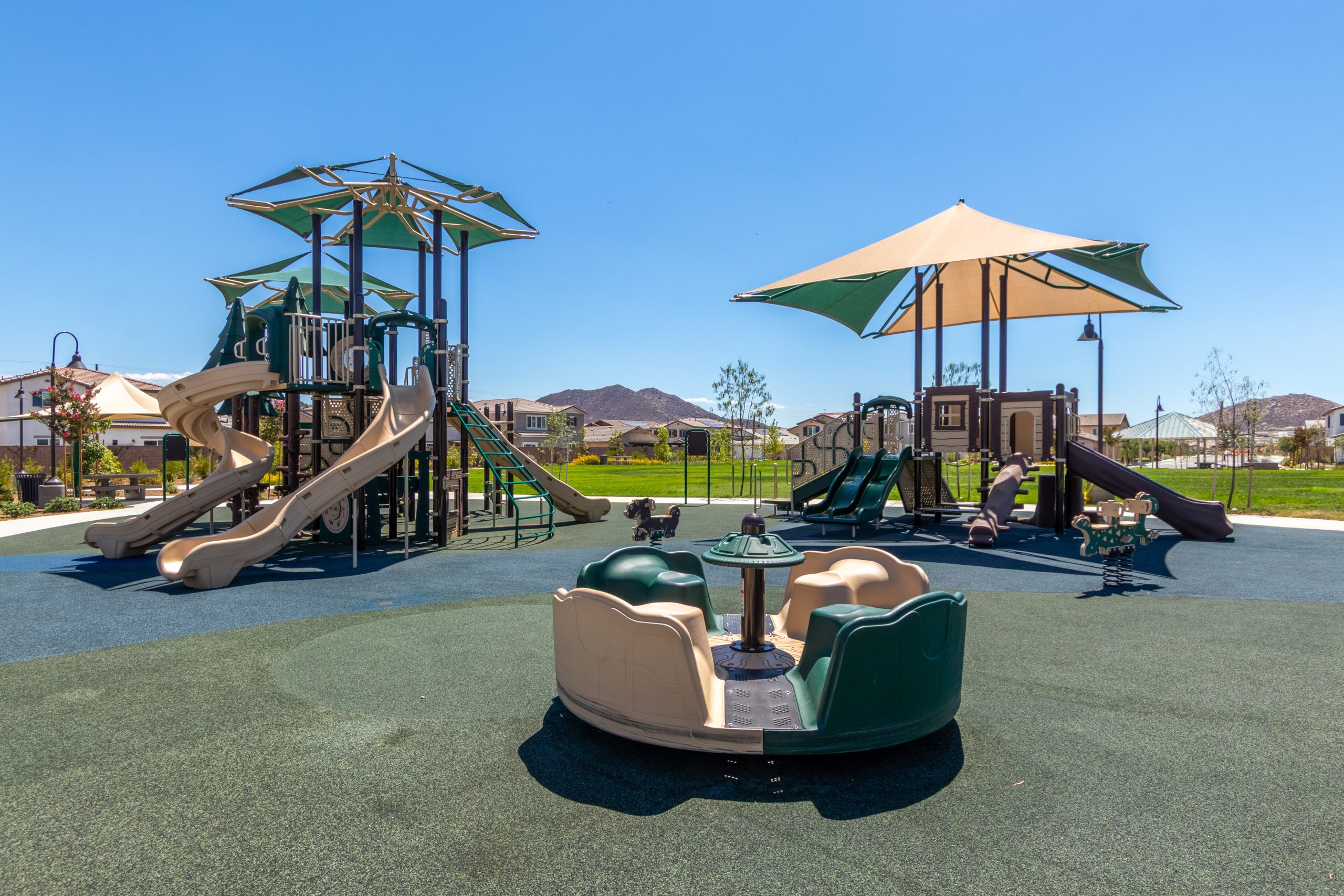 Interactive spinners with a partial slide in the background at La Pradera South Park in Winchester, CA, part of the forest-inspired playground installed by Pacific Play Systems.